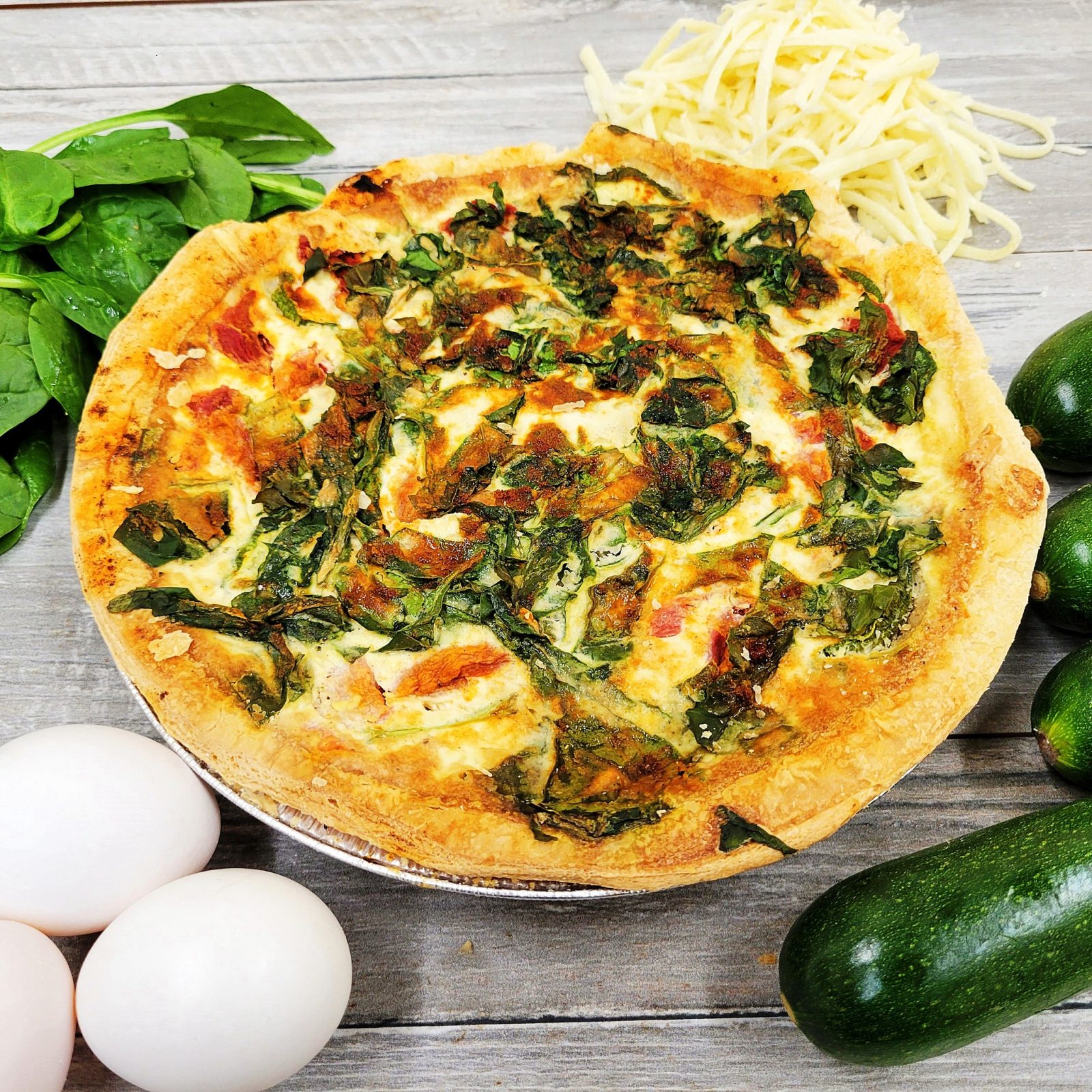 A pizza is sitting on a table next to eggs and vegetables.