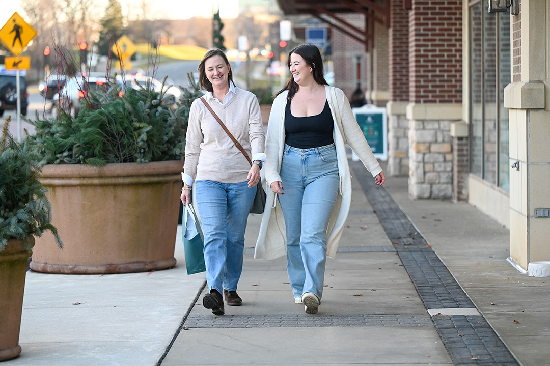 Two women walking on a sidewalk.