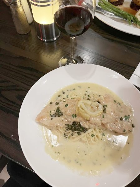 A plate of fish with sauce and wine on a table.
