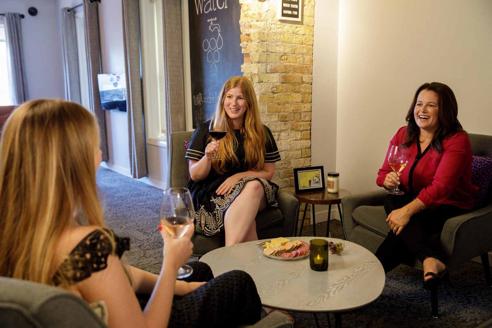Three women sitting in a room drinking wine.