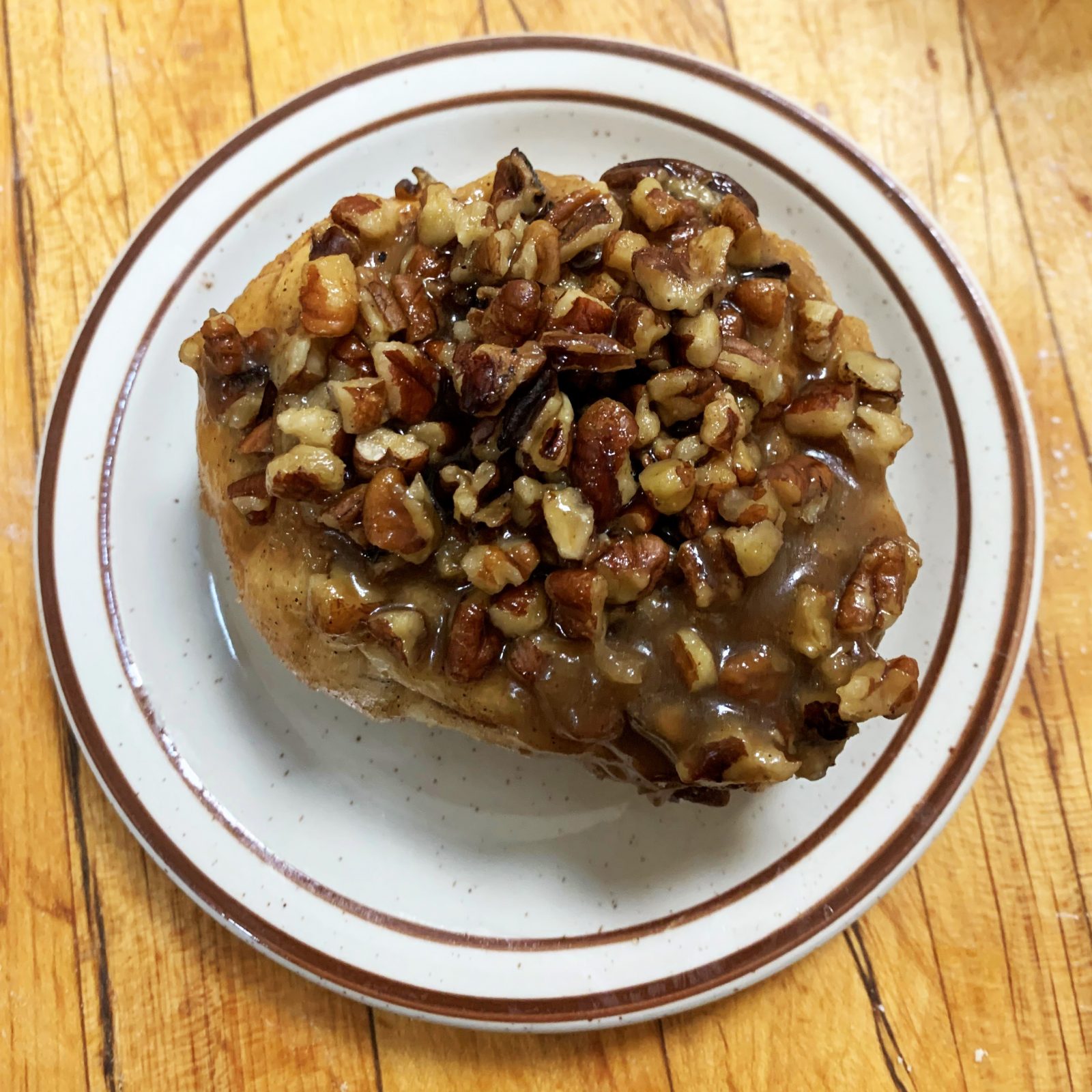 A plate with a cinnamon roll and pecans on it.
