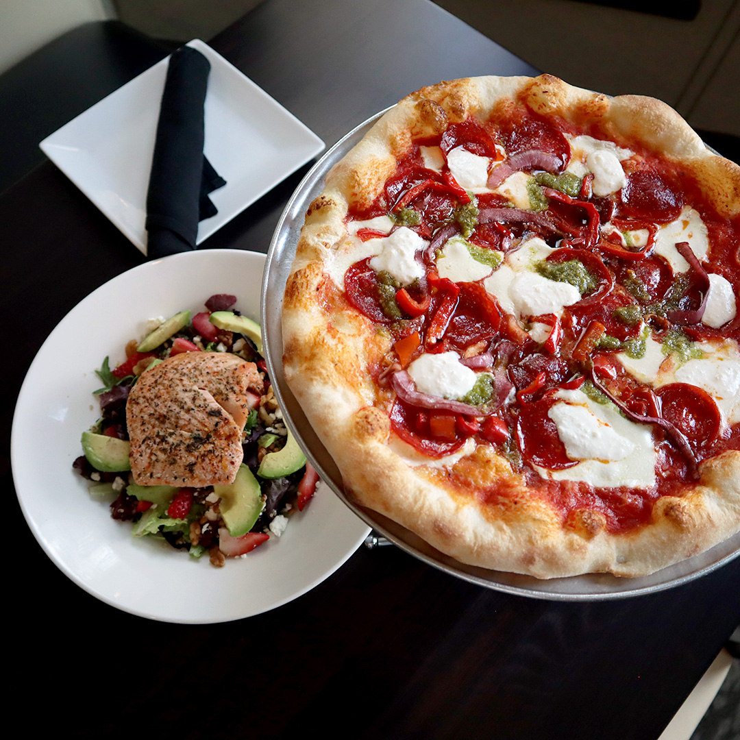 A pizza on a plate next to a salad on a table.