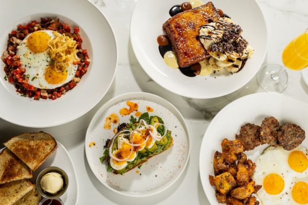 A delightful Easter brunch spread featuring eggs over hash, stuffed toast with bananas, and avocado toast with eggs, alongside two plates of seasoned potatoes. Orange juice rounds out this festive family gathering.