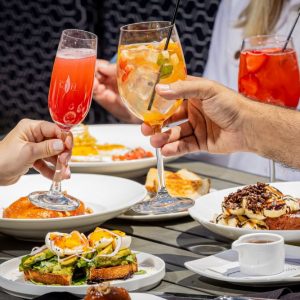People clinking glasses over a table laden with delightful brunch dishes, such as avocado toast and French toast, celebrating Easter with joy.