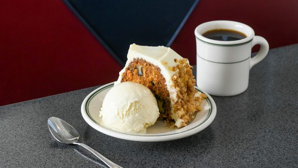 A slice of carrot cake with nuts, a scoop of vanilla ice cream, and a cup of coffee sit invitingly on a speckled counter, making for perfect springtime treats.