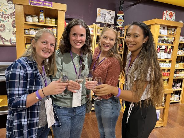 Four women holding wine in the National Mustard Museum during DMBA's 2023 Sip & Stroll Wine Walk