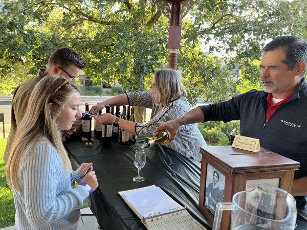 DMBA's 2023 Sip & Stroll Wine Walk: two people serve as two people try wine at the Rowley House Museum