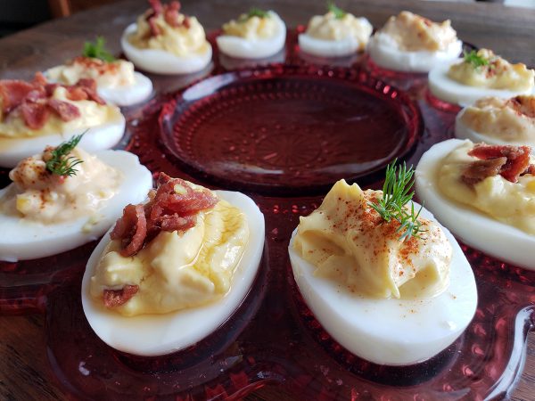 A plate of deviled eggs topped with bacon and garnished with herbs.