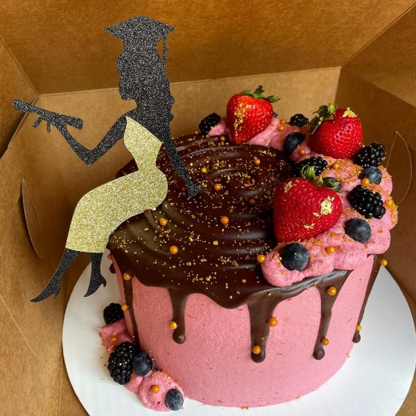 A celebration cake with pink frosting, chocolate ganache topping, and adorned with fresh berries and a silhouette topper.