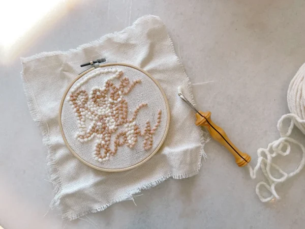 Embroidery hoop with a partially completed floral design, a needle, and white thread on a table.