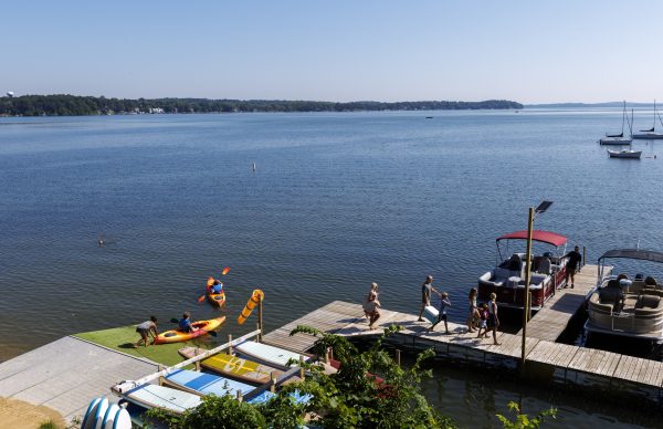 People are kayaking, walking on the Marshall Park dock, and boarding boats from Marshall Boats Board and Rentals, with trees and sailboats visible in the background under a clear sky.