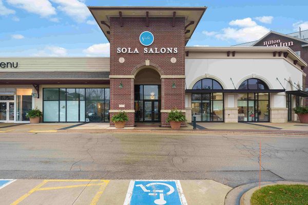 Exterior view of a Sola Salons storefront with large windows, brick facade, and accessible parking space in front.