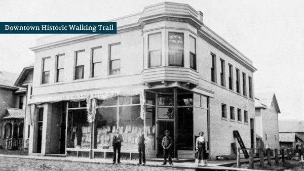 A historic black-and-white photo shows a two-story corner building with five people standing in front, labeled "Downtown Historic Walking Trail.