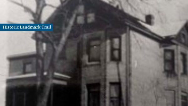 Black and white photo of an old two-story house with a sloped roof and a bare tree in front. A blue label reads, "Historic Landmark Trail.