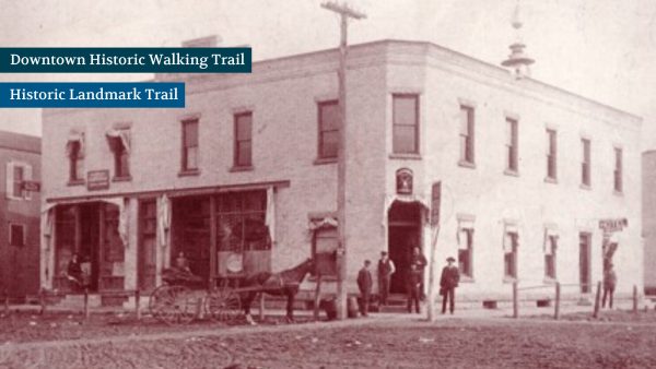 Vintage photo of a two-story brick building with people and a horse-drawn carriage in front. Signs for "Downtown Historic Walking Trail" and "Historic Landmark Trail" are overlaid.
