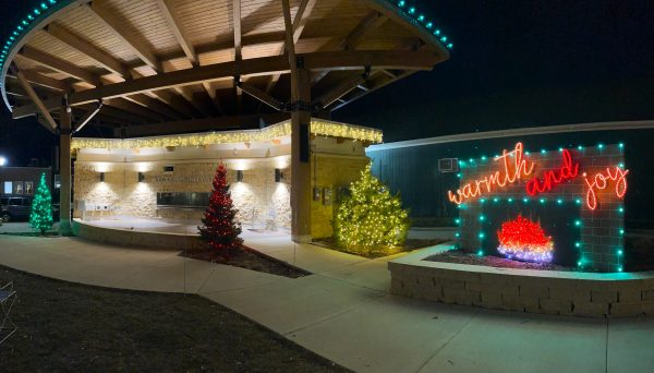 Outdoor area decorated with Christmas lights, including lit trees and a "warmth and joy" fireplace sign at night under a wooden canopy—perfect ambiance after visiting nearby vegetarian restaurants.