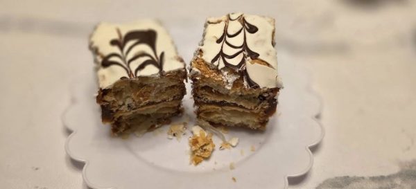 Two pieces of layered pastry with white icing and chocolate decorative lines are placed on a white plate at Toro Y Pampa, an Argentinian restaurant, with crumbs scattered around them.