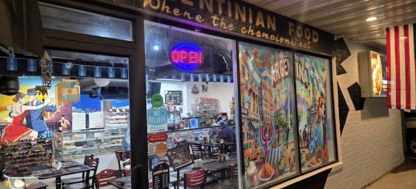 Exterior view of Toro Y Pampa, an Argentinian restaurant at night, featuring a neon "Open" sign, colorful murals on the windows, and tables visible inside.
