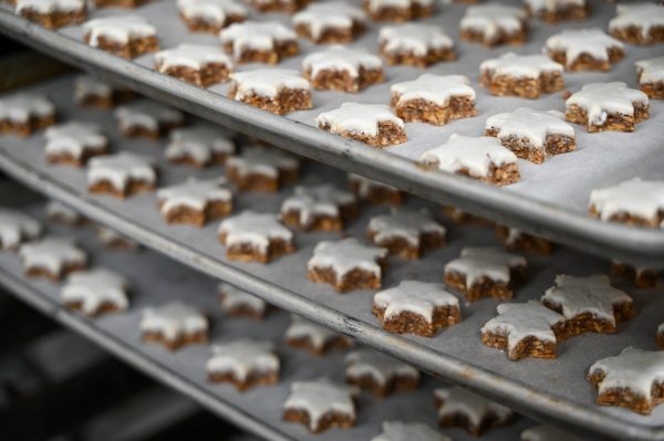 Multiple trays of star-shaped cookies with white icing are arranged on baking sheets, ready for or just out of baking in an industrial oven or kitchen.