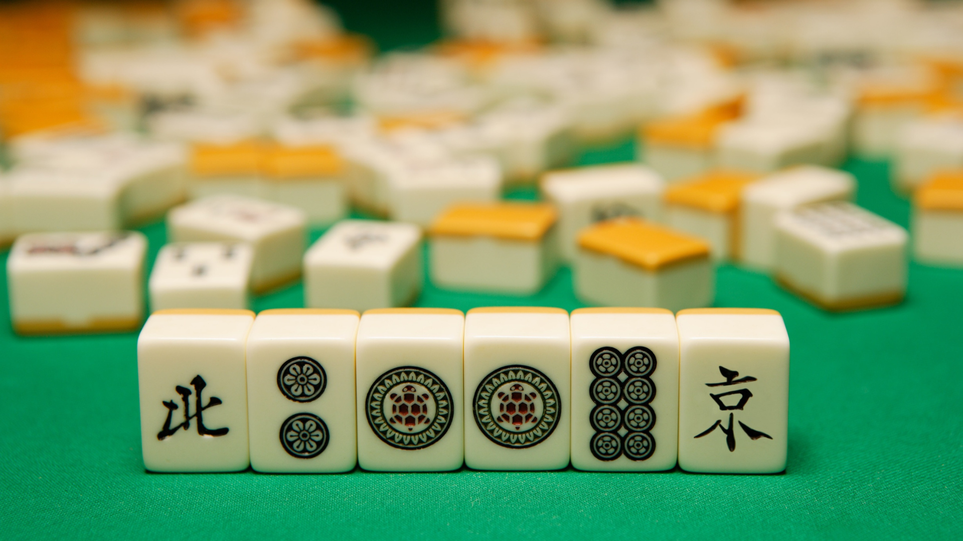 Mahjong tiles arranged in a row on a green table, with additional tiles scattered in the background.