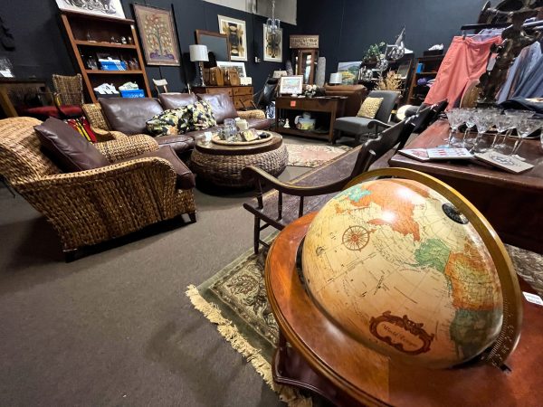 A room filled with vintage furniture and decor, curated by RTC Estate Sales, including a leather sofa, wicker chairs, assorted tables, shelves, and a large globe on a wooden stand in the foreground.