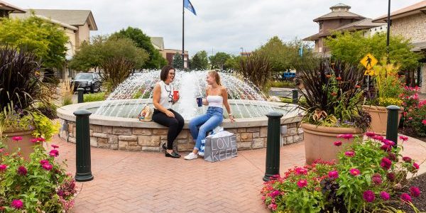 two women sitting on a fountain talking and drinking
