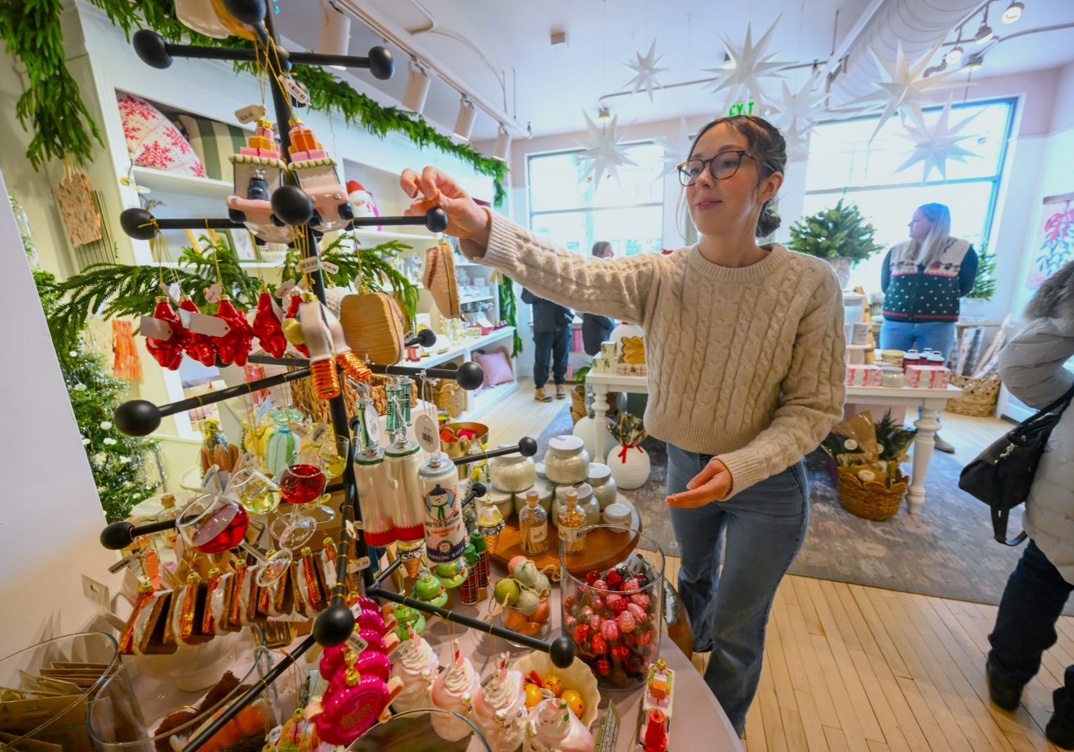 A woman arranges Christmas ornaments on a display tree in a brightly lit shop, making it a festive stop for your Middleton Bucket List and one of the charming things to do in Middleton during the holiday season.
